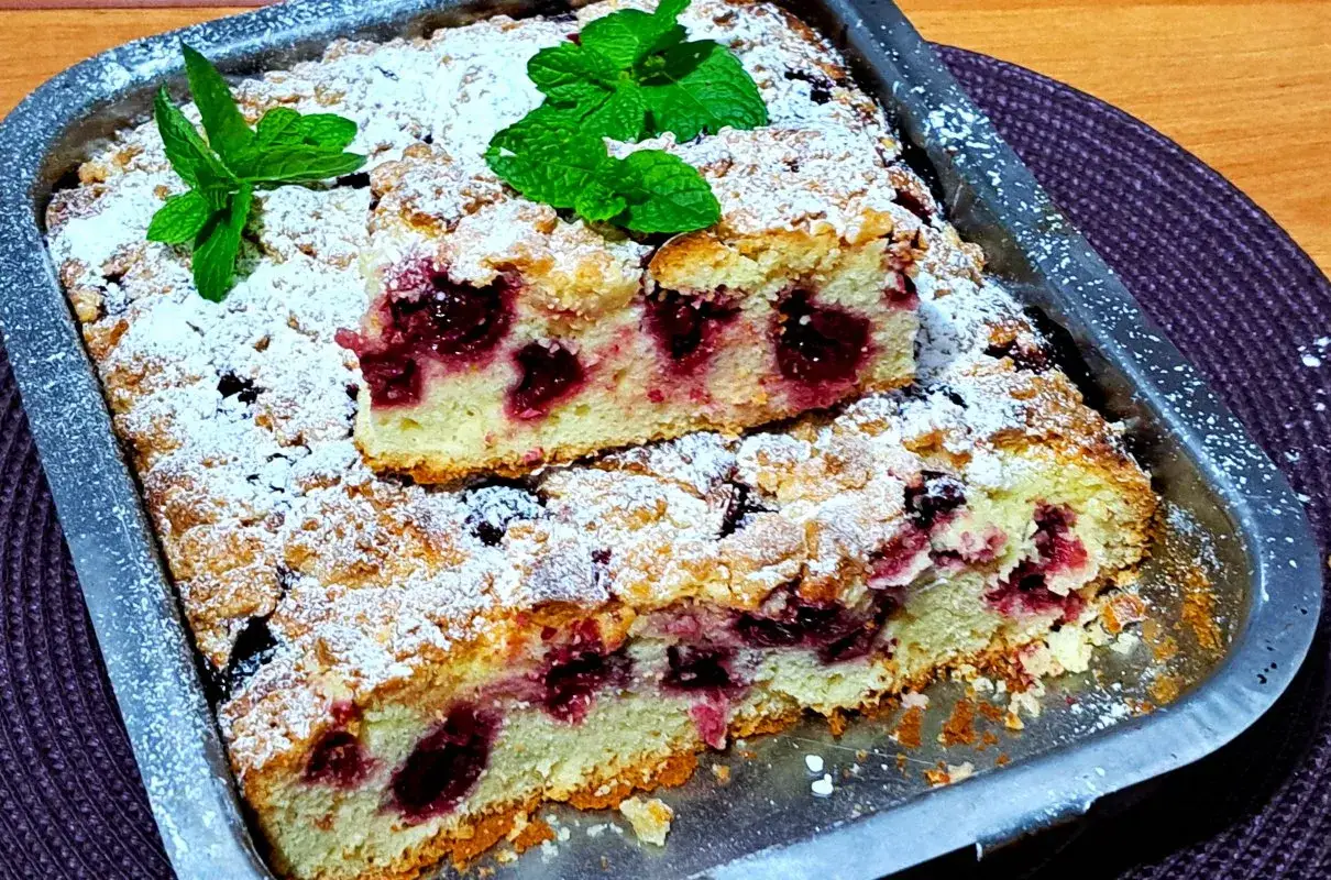 Puszyste ciasto z wiśniami, posypane cukrem pudrem i ozdobione listkami mięty. Idealne na letnie popołudnie.