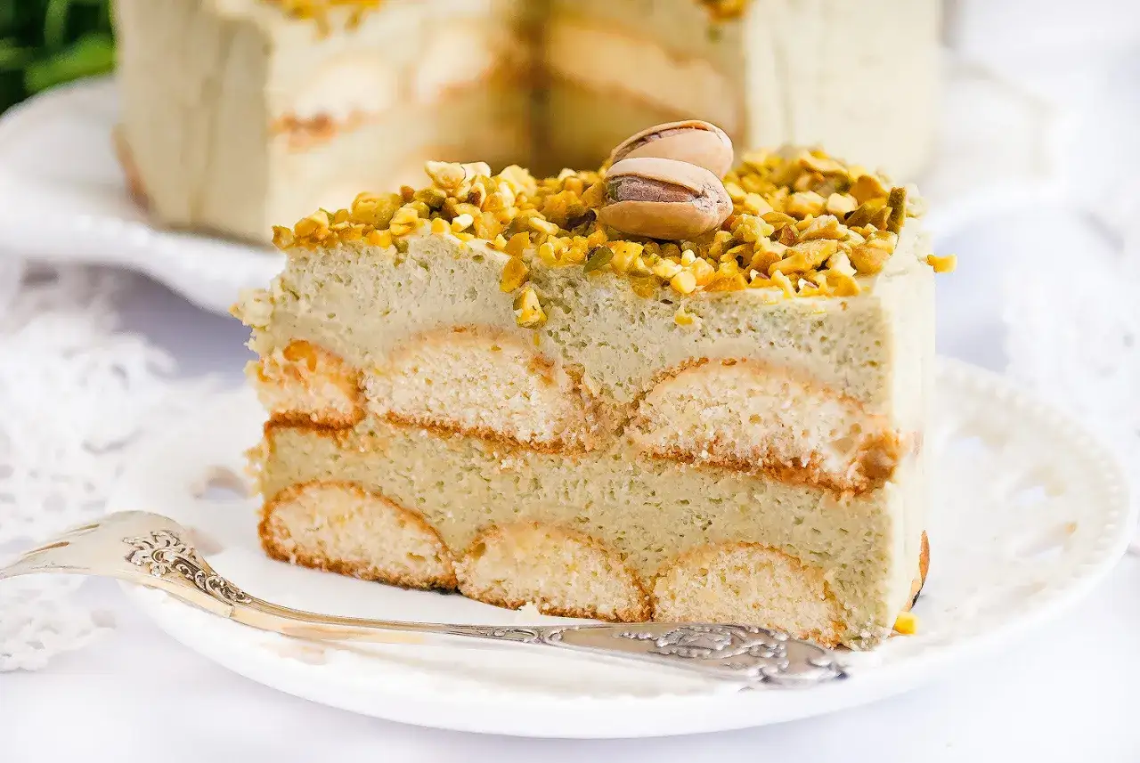 Pyszne ciasto pistacjowe z mascarpone, przełożone biszkoptami i posypane orzechami. Idealne na deser.