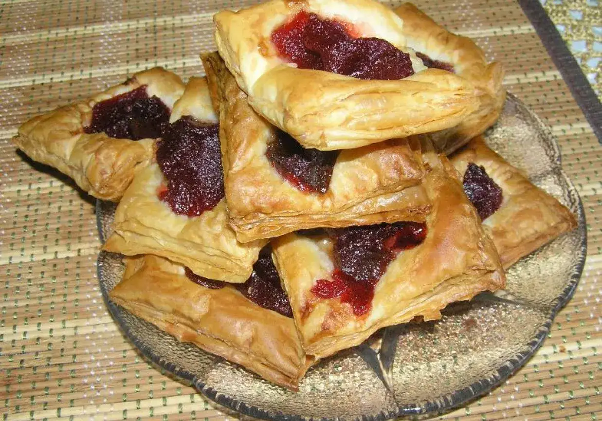 Chrupiące ciastka z marmoladą z ciasta francuskiego ułożone na szklanym talerzu.