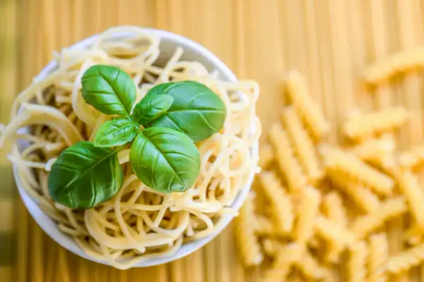 Miseczka spaghetti z bazylią, obok rozsypane fusilli. To klasyczne danie, gdzie co to jest semolina z pszenicy durum, stanowi podstawę.