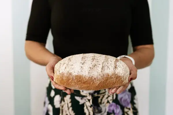 Kobieta trzyma bochenek chleba razowego. Zastanawiasz się, ile kcal ma kromka chleba razowego? Ten pyszny chleb może być częścią zdrowej diety.