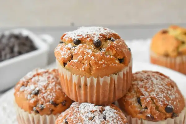 Pyszne muffinki z kawałkami czekolady, posypane cukrem pudrem, kuszą swoim wyglądem. Idealne na deser!