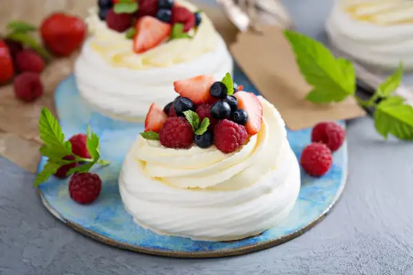 Beza pavlova z mascarpone, udekorowana malinami, borówkami i truskawkami. Letni deser na błękitnym talerzu.
