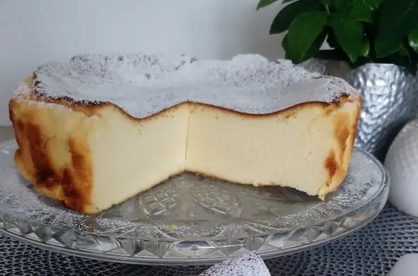 Puszyste ciasto z mlekiem skondensowanym, oprószone cukrem pudrem, prezentuje się apetycznie na szklanej paterze.