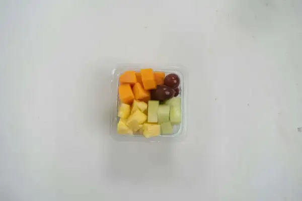 Pudełko z pokrojonymi owocami: ananas, melon, papaja i winogrona. Idealna przekąska, jeśli zastanawiasz się, czy mus owocowy można do samolotu.