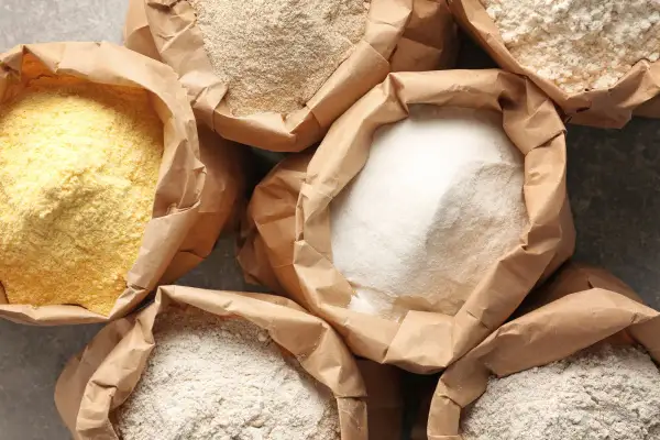 Różne rodzaje mąk w papierowych torbach. Zastanawiasz się, ile glutenu ma mąka pszenna? Tutaj znajdziesz odpowiedź.