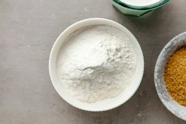 Biała miska z mąką, obok miska z brązowym cukrem i szklanka mleka. Zastanawiasz się, ile szklanek ma kilogram mąki?