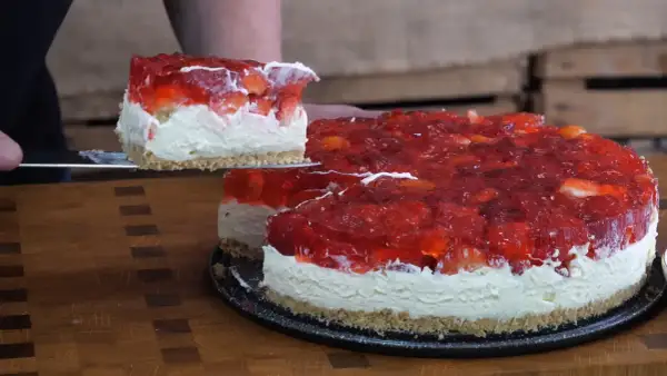 Krojony tort z galaretką truskawkową i bitą śmietaną na spodzie z ciastek.
