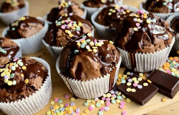 Czekoladowe muffiny polane lukrem i posypane kolorową posypką. Proste sposoby, jak dekorować muffiny, by wyglądały apetycznie.