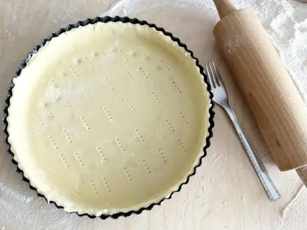 Surowe ciasto kruche w formie do tarty, widelec i wałek. Czy do kruchego ciasta daje się proszek do pieczenia?