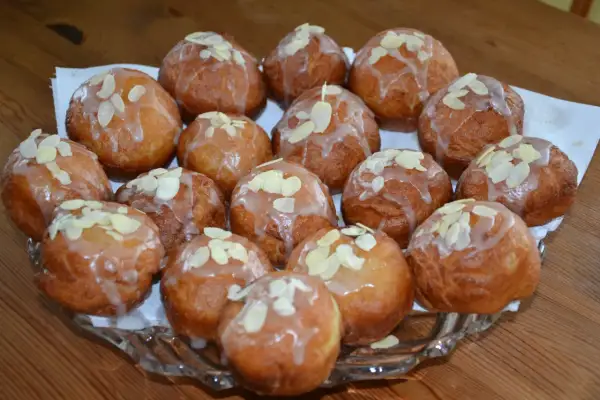 Pyszne pączki z adwokatem, polane lukrem i posypane płatkami migdałów, ułożone na szklanej paterze.