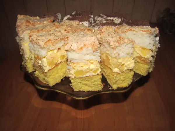 Pyszne ciasto z ananasem i kokosem, z bezą i kremem, pokrojone na kawałki na paterze.